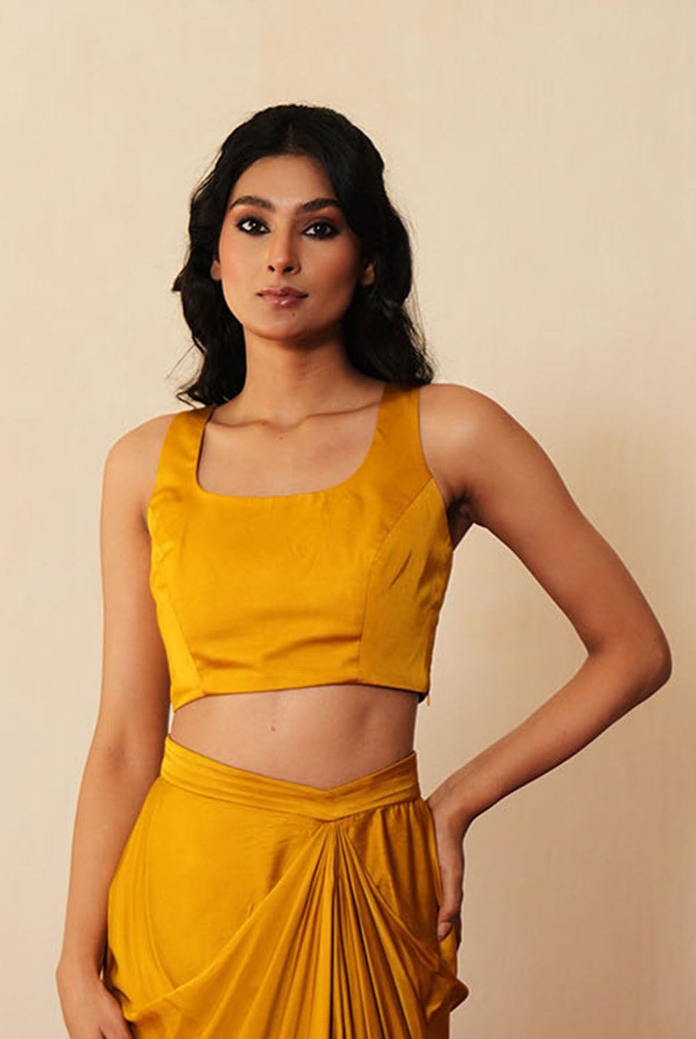 Woman in a golden yellow traditional outfit standing againsta beige wall on a red carpet.