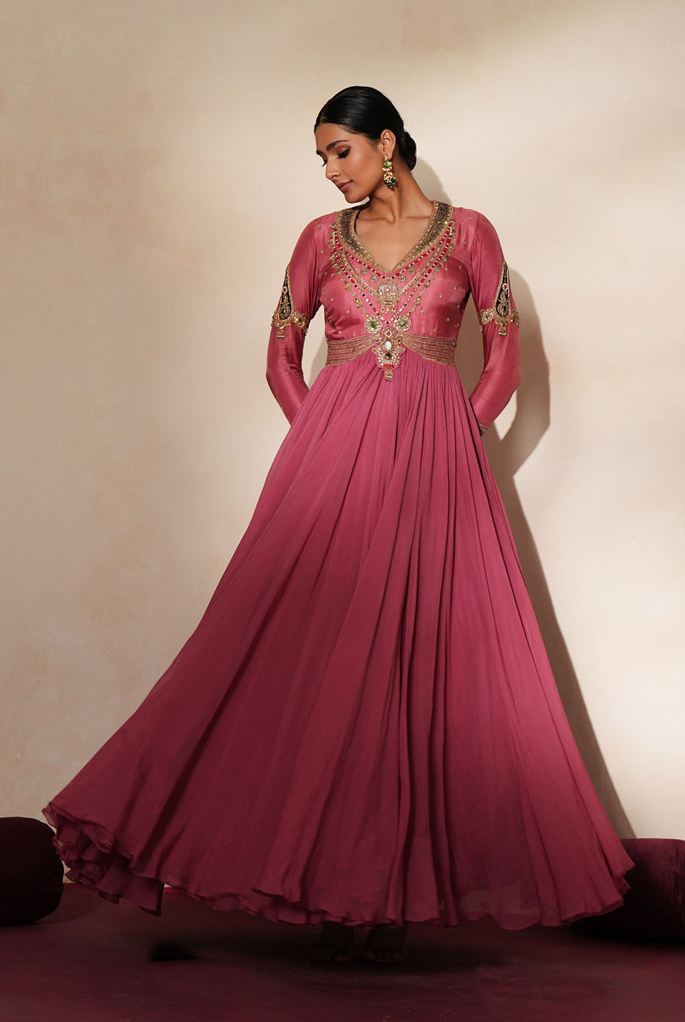 Woman in a mauve pink traditional outfit standing againsta beige wall on a red carpet.