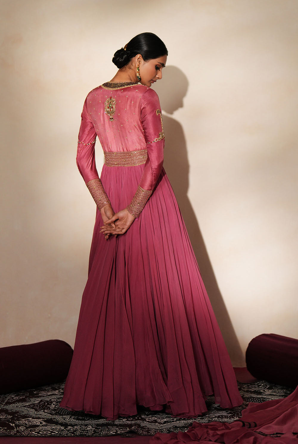 Woman in a mauve pink traditional outfit standing againsta beige wall on a red carpet.