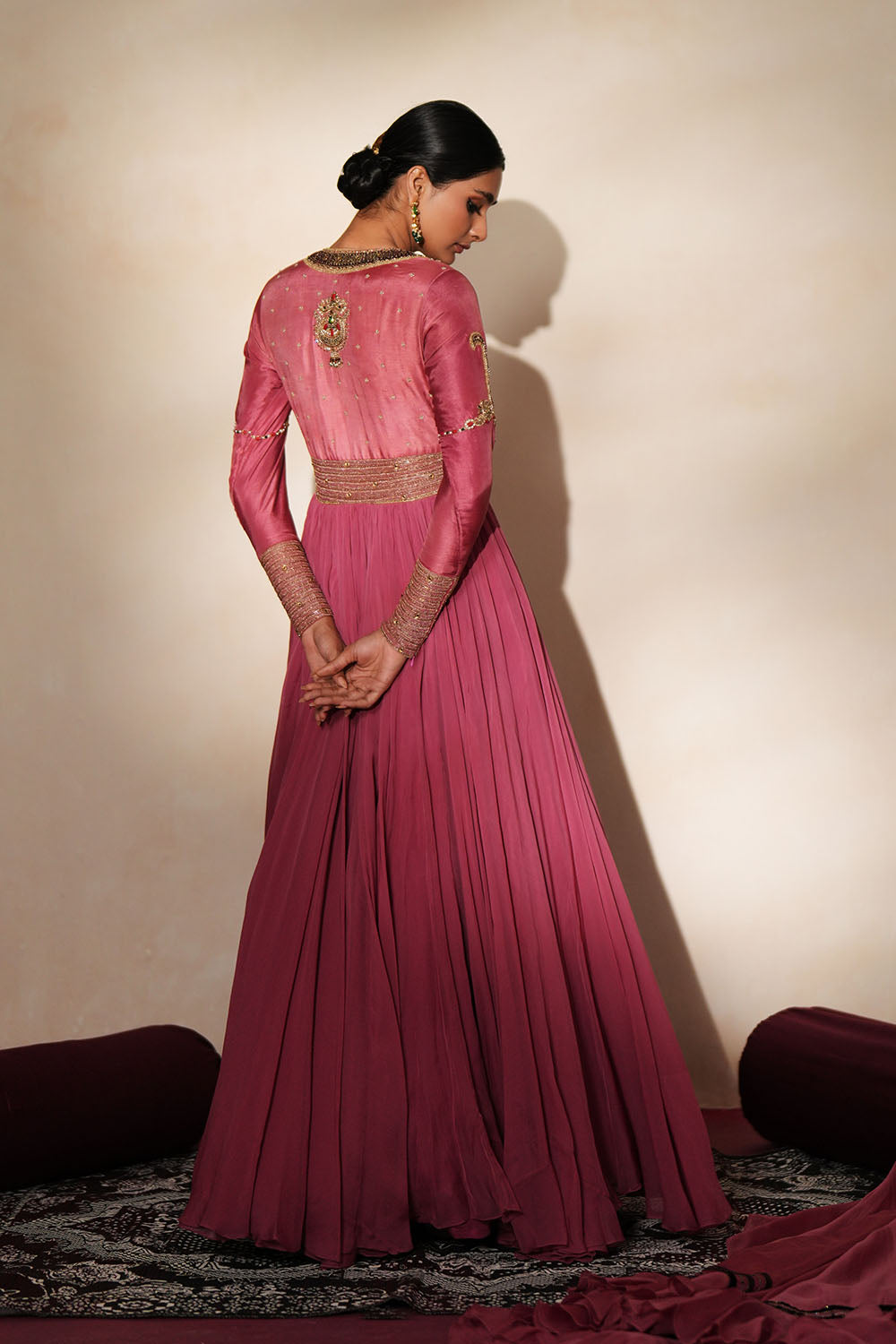 Woman in a mauve pink traditional outfit standing againsta beige wall on a red carpet.