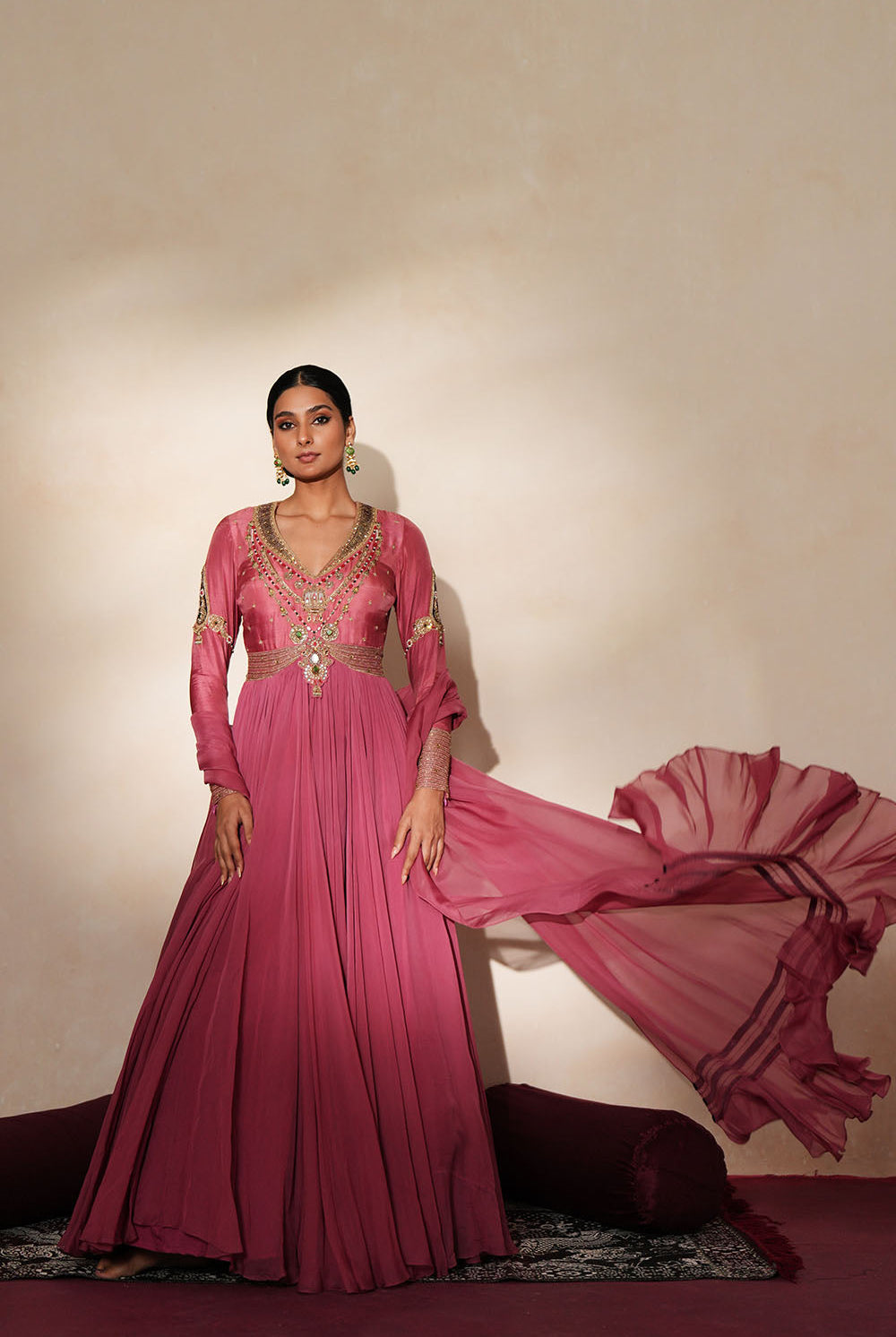 Woman in a mauve pink traditional outfit standing againsta beige wall on a red carpet.