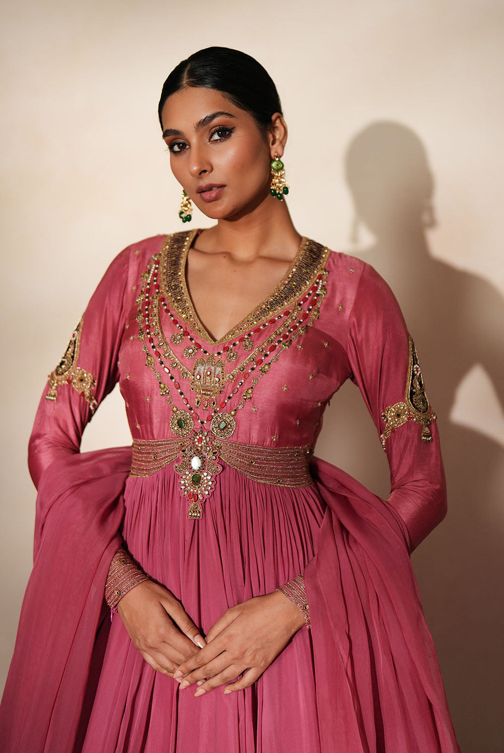 Woman in a mauve pink traditional outfit standing againsta beige wall on a red carpet.
