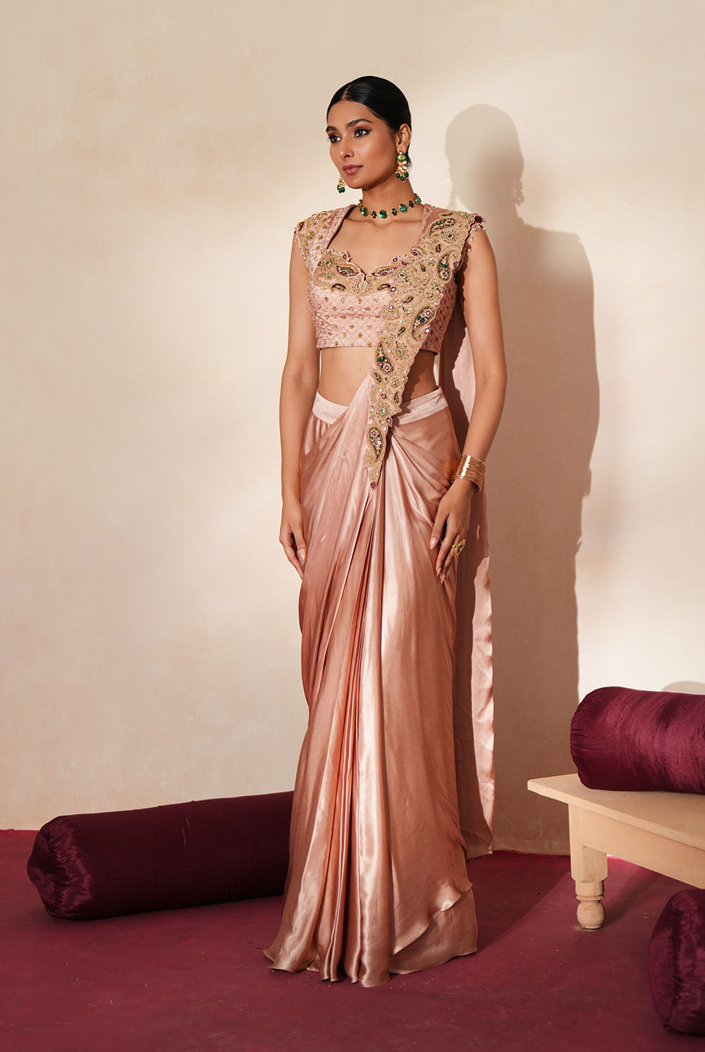 Woman in a soft pink traditional outfit standing againsta beige wall on a red carpet.