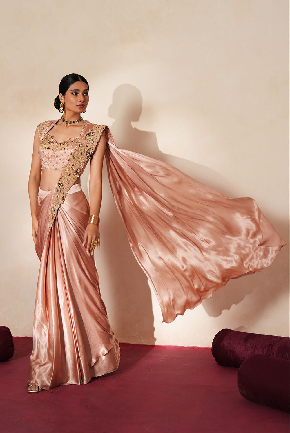 Woman in a soft pink traditional outfit standing againsta beige wall on a red carpet.