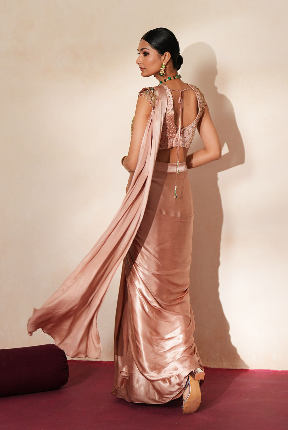 Woman in a soft pink traditional outfit standing againsta beige wall on a red carpet.