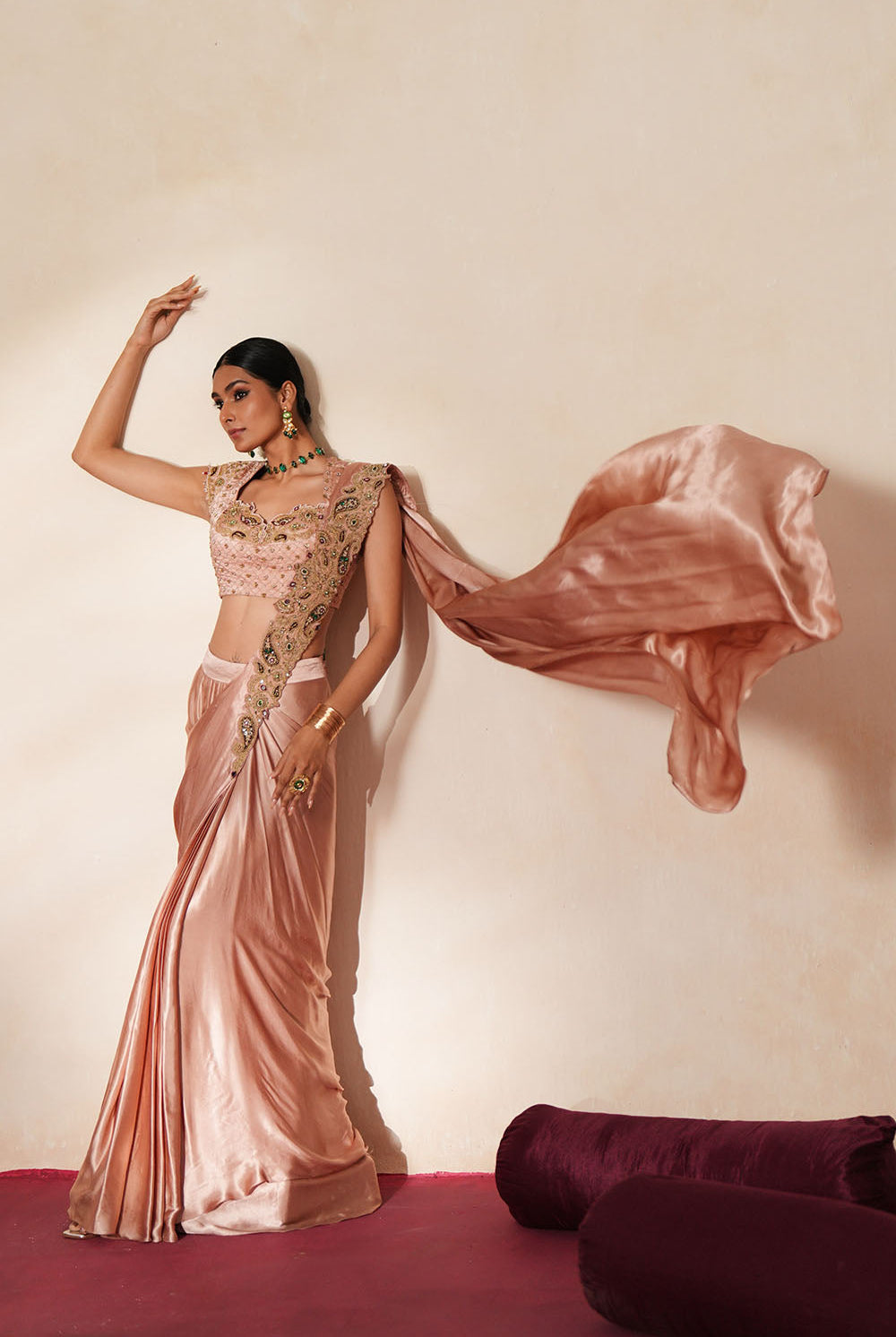 Woman in a soft pink traditional outfit standing againsta beige wall on a red carpet.