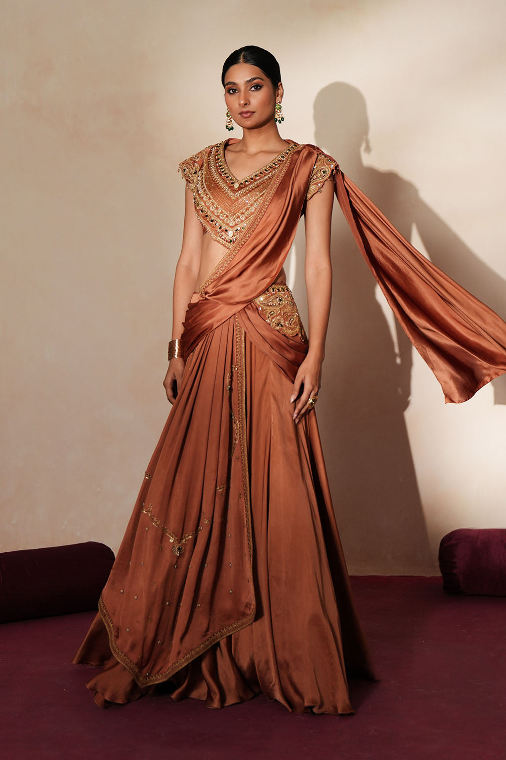 Woman in a metallic mocha traditional outfit standing againsta beige wall on a red carpet.