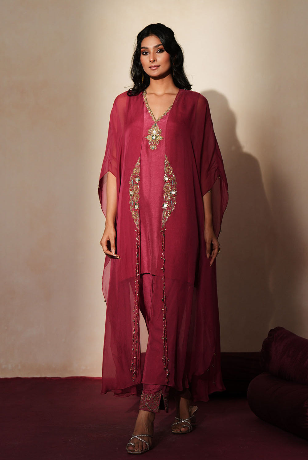 Woman in a mauve pink traditional outfit standing againsta beige wall on a red carpet.