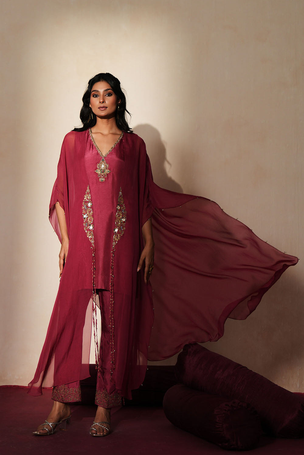 Woman in a mauve pink traditional outfit standing againsta beige wall on a red carpet.