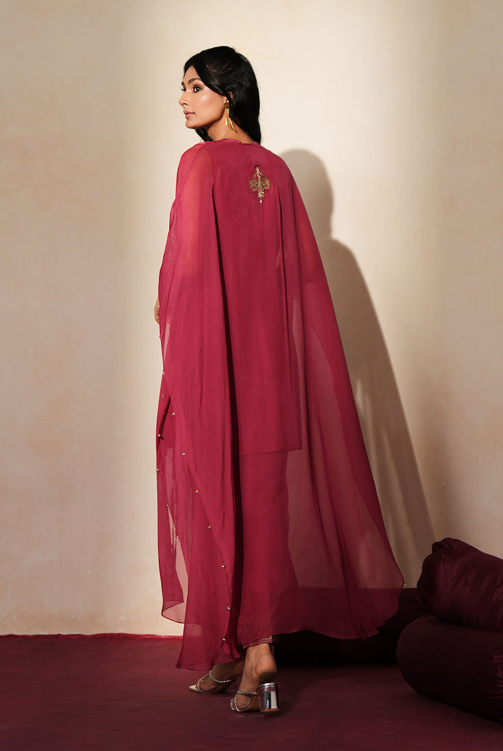 Woman in a mauve pink traditional outfit standing againsta beige wall on a red carpet.