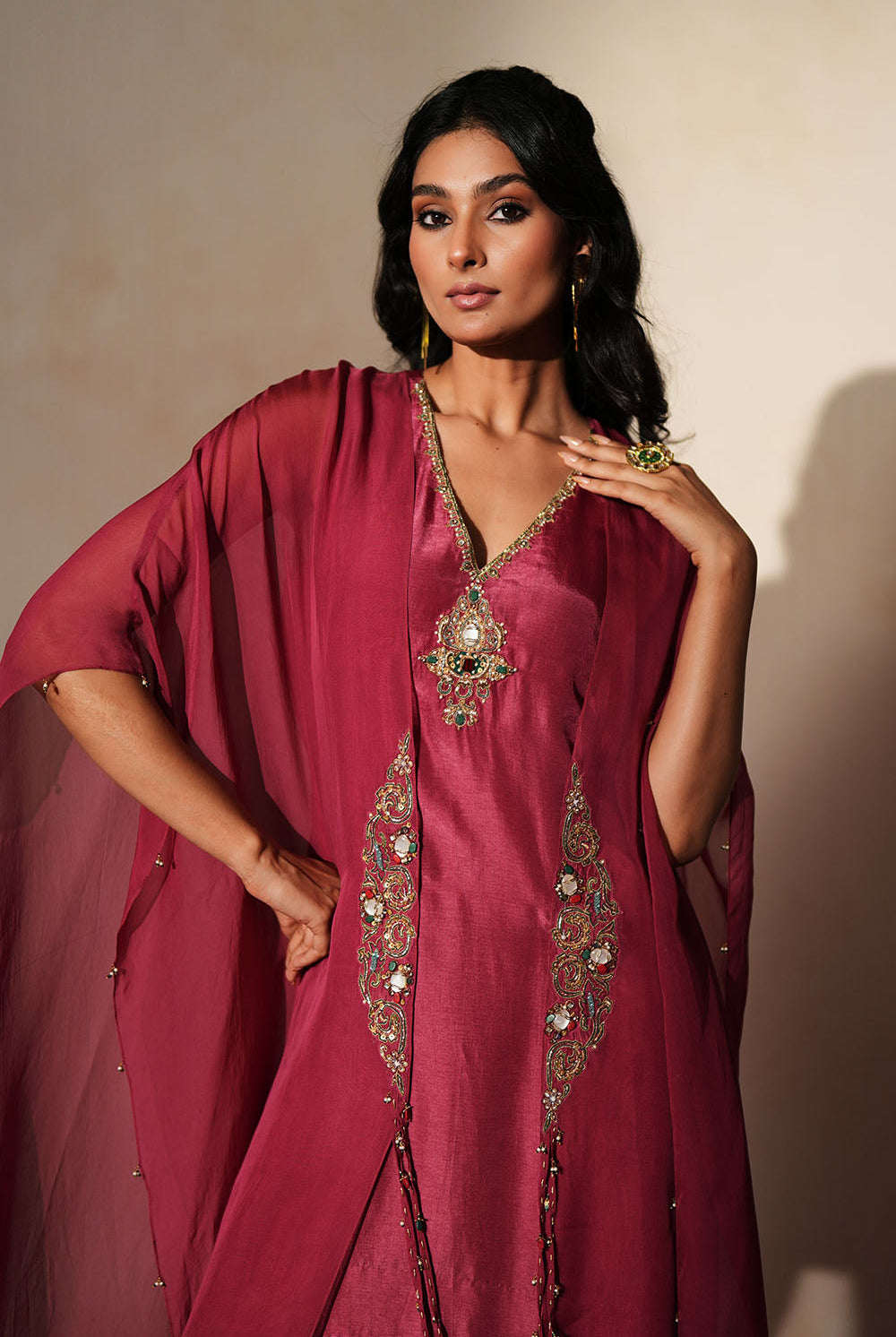 Woman in a mauve pink traditional outfit standing againsta beige wall on a red carpet.