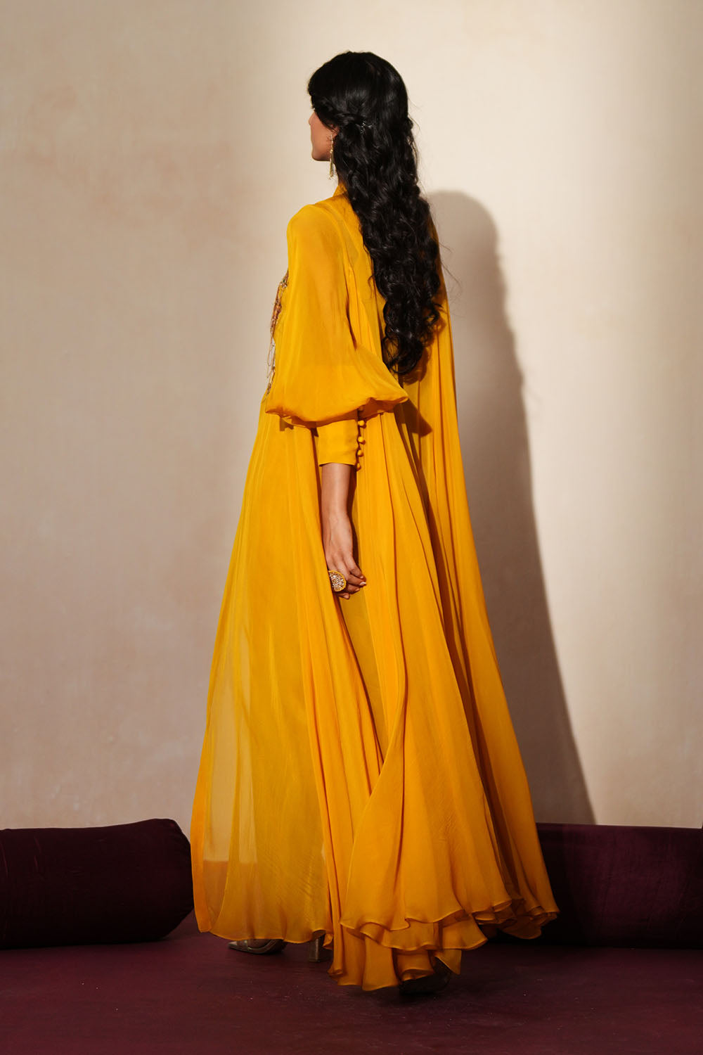 Woman in a golden yellow traditional outfit standing againsta beige wall on a red carpet.