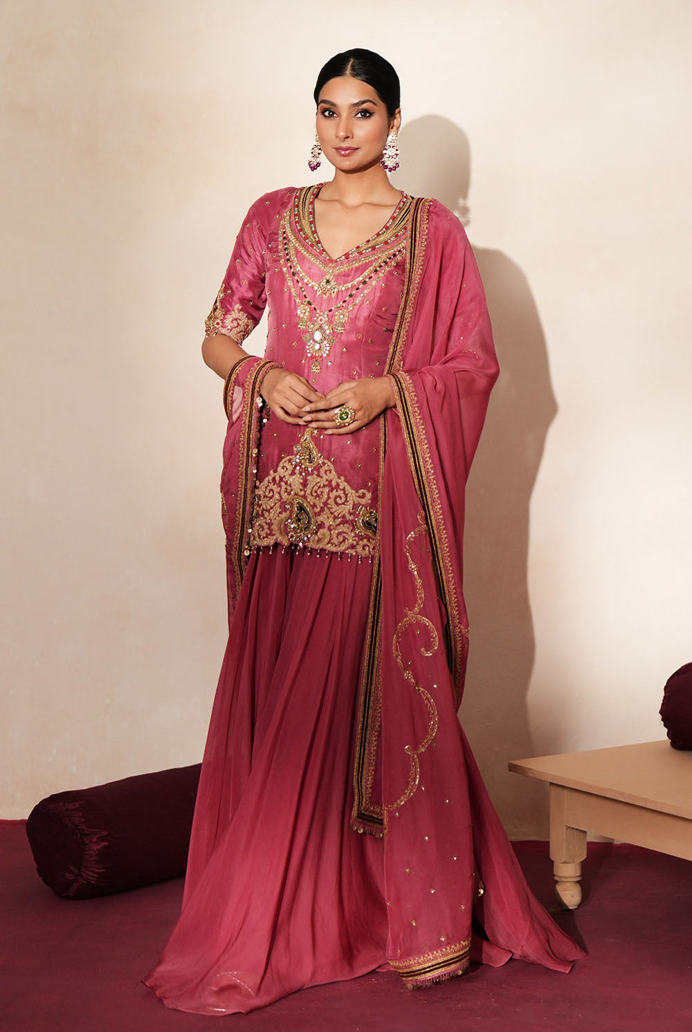 Woman in a mauve pink traditional outfit standing againsta beige wall on a red carpet.