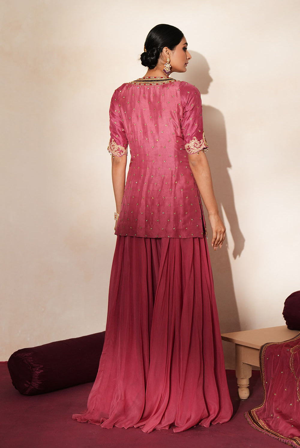 Woman in a mauve pink traditional outfit standing againsta beige wall on a red carpet.