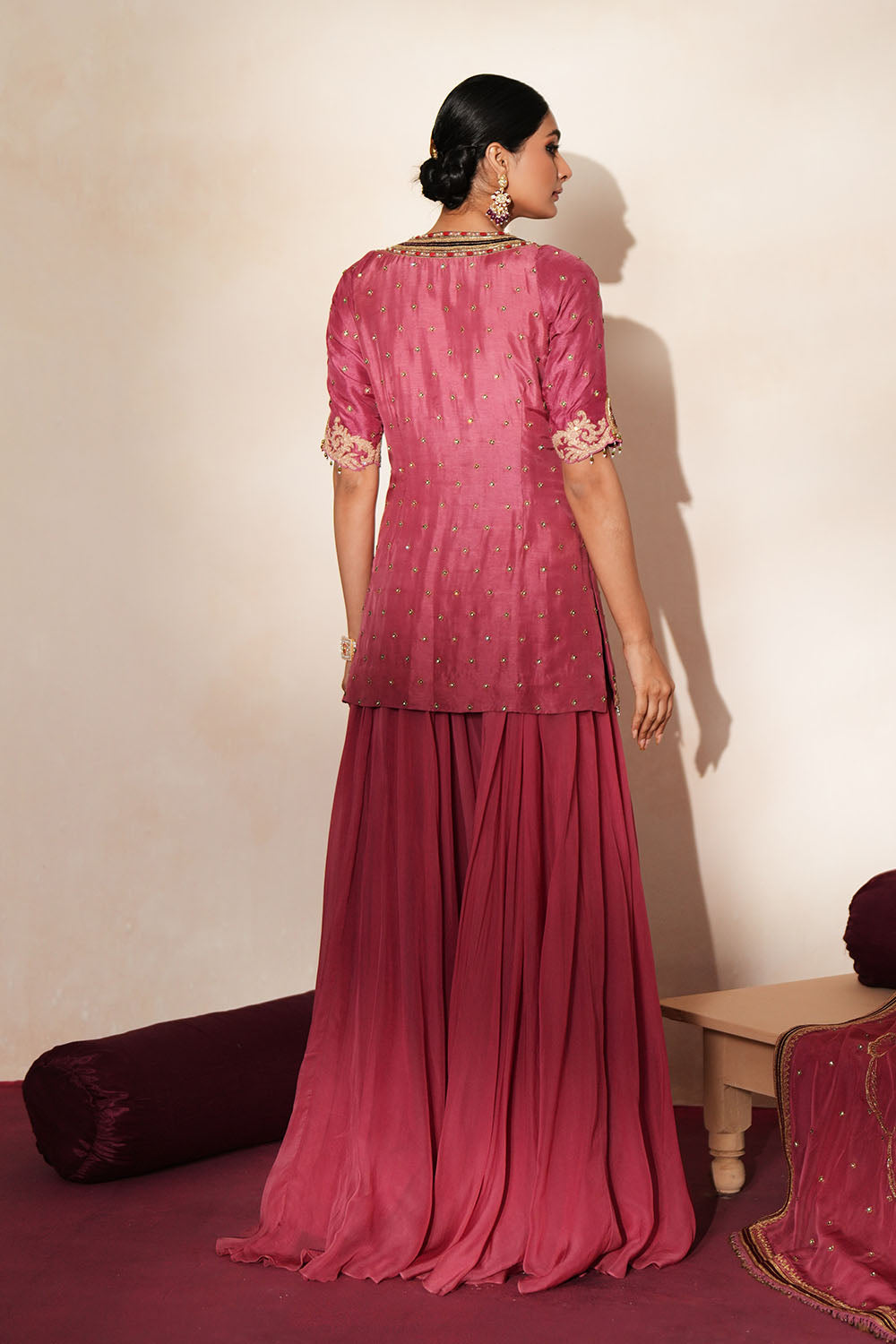 Woman in a mauve pink traditional outfit standing againsta beige wall on a red carpet.