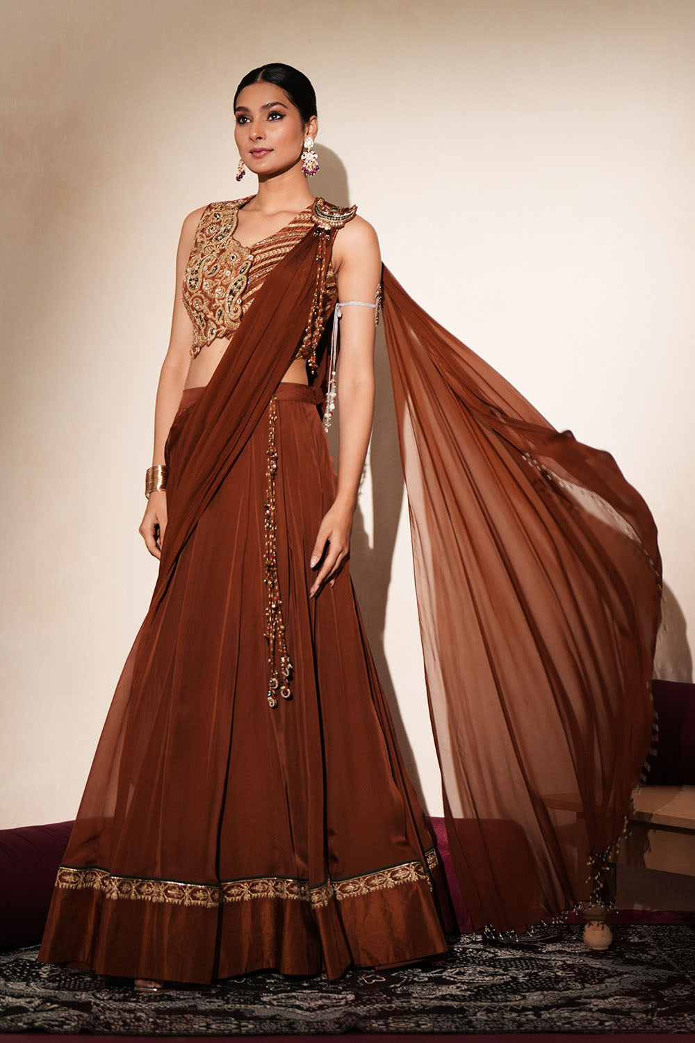 Woman in a mettalic brown traditional outfit standing againsta beige wall on a red carpet.