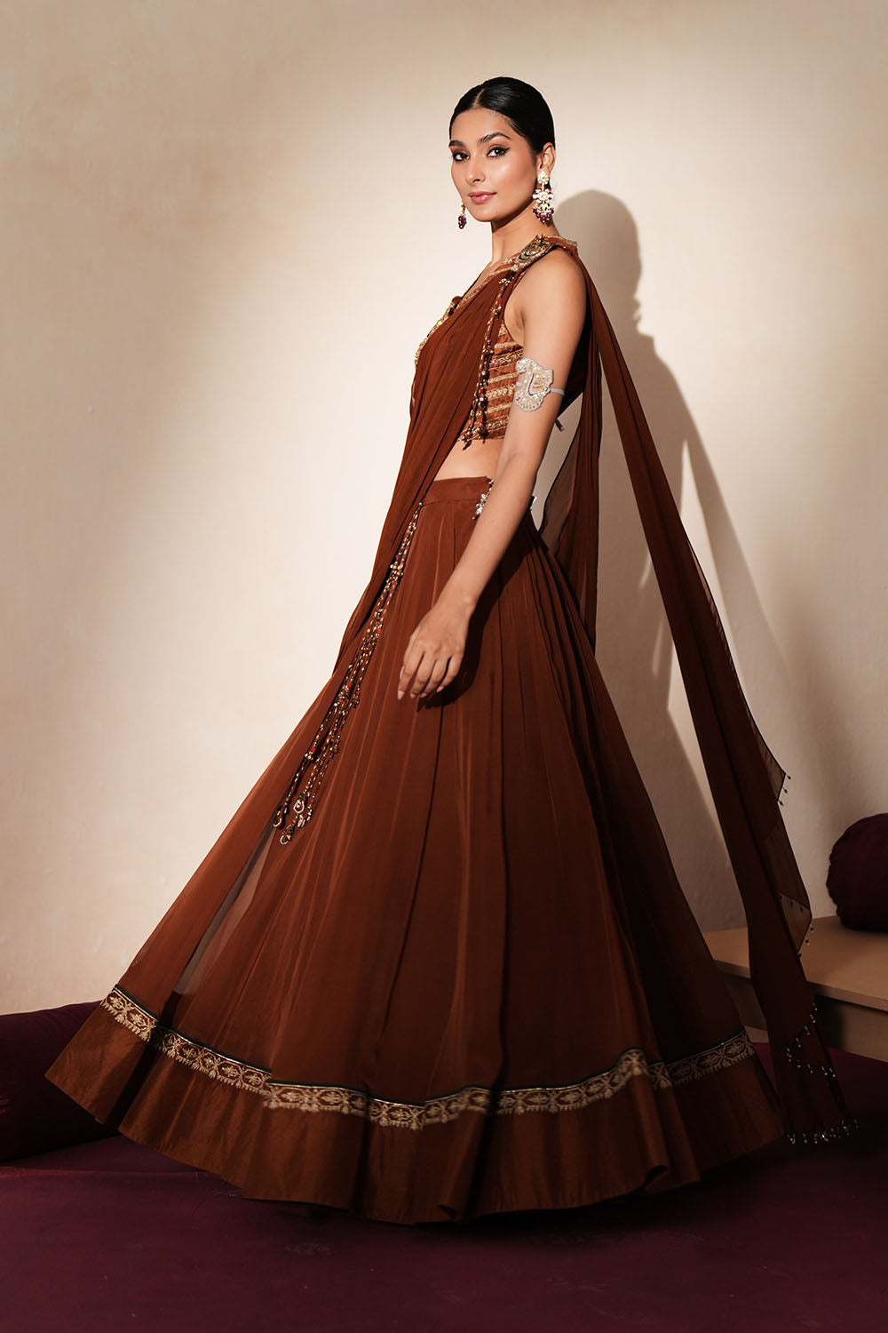 Woman in a mettalic brown traditional outfit standing againsta beige wall on a red carpet.