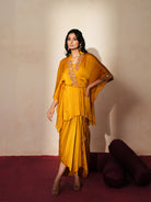 Woman in a golden yellow traditional outfit standing againsta beige wall on a red carpet.