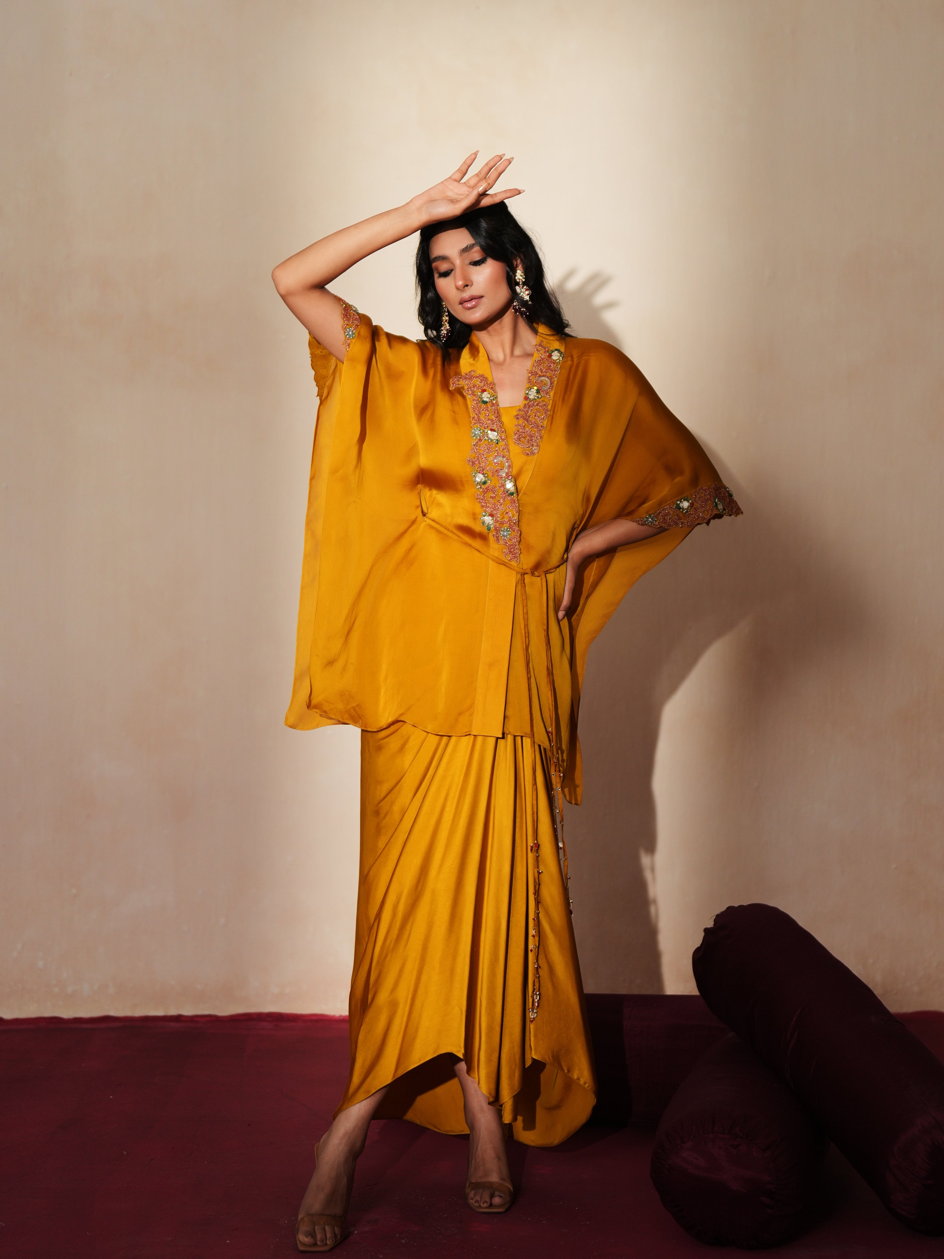 Woman in a golden yellow traditional outfit standing againsta beige wall on a red carpet.