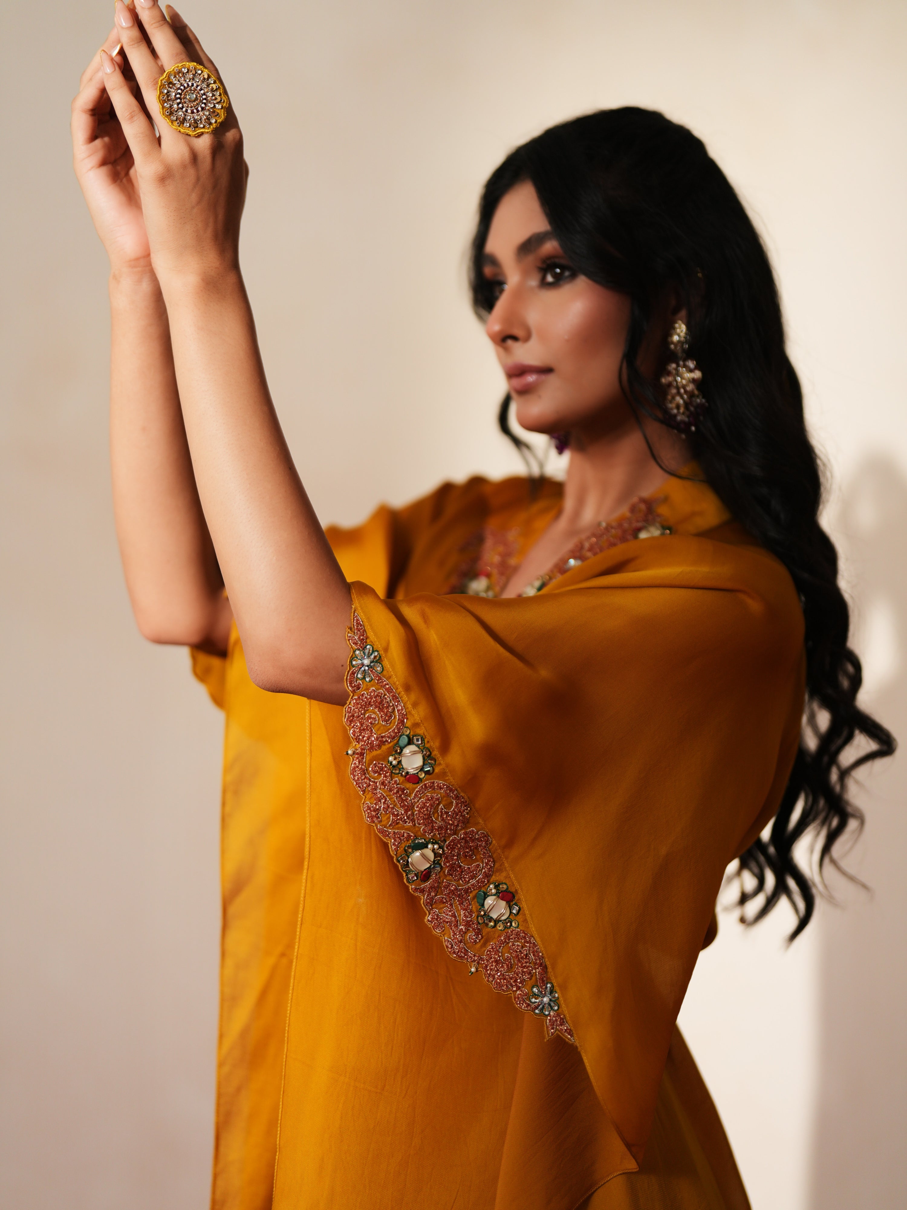 Woman in a golden yellow traditional outfit standing againsta beige wall on a red carpet.