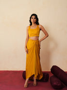 Woman in a golden yellow traditional outfit standing againsta beige wall on a red carpet.