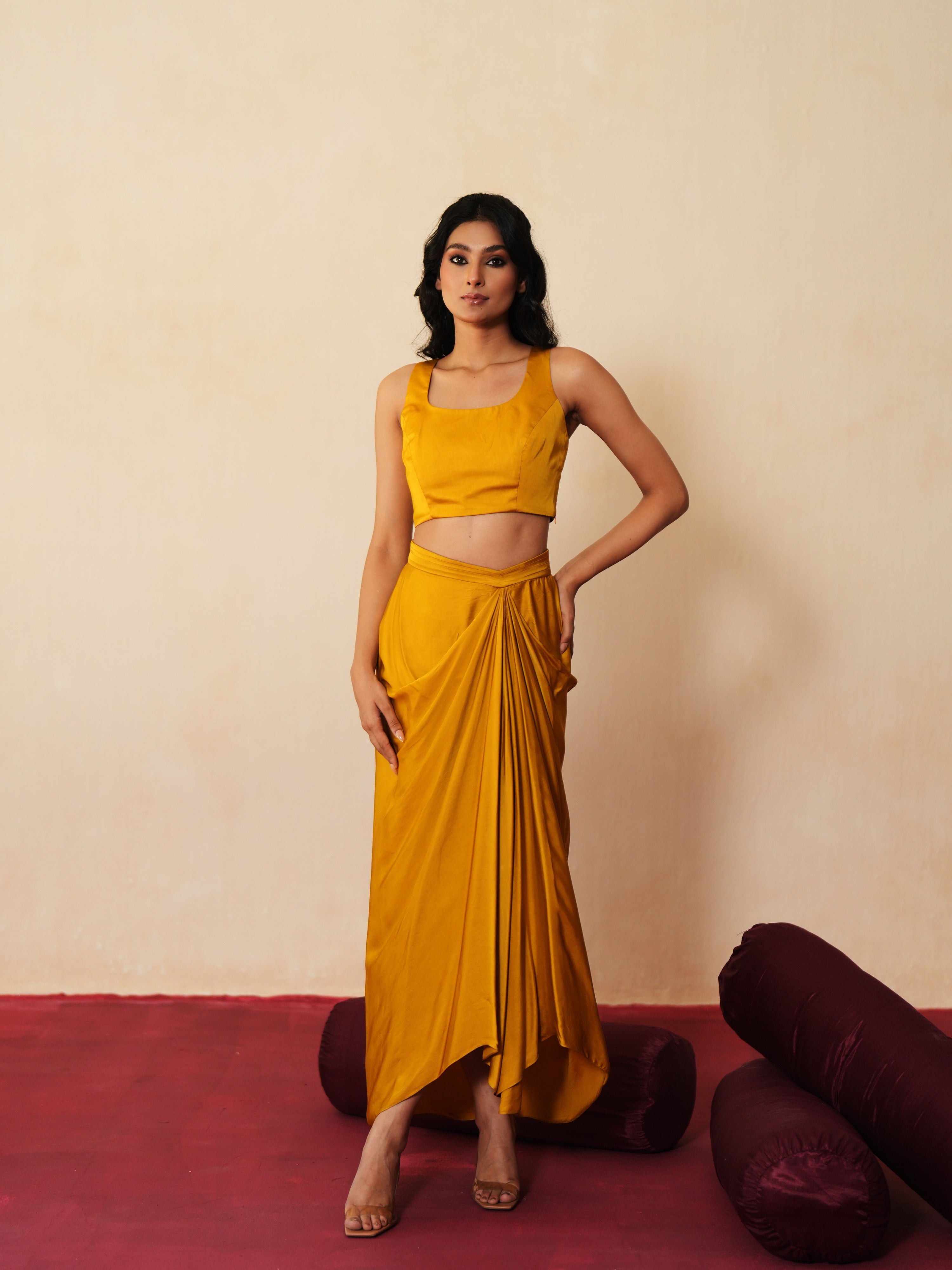 Woman in a golden yellow traditional outfit standing againsta beige wall on a red carpet.