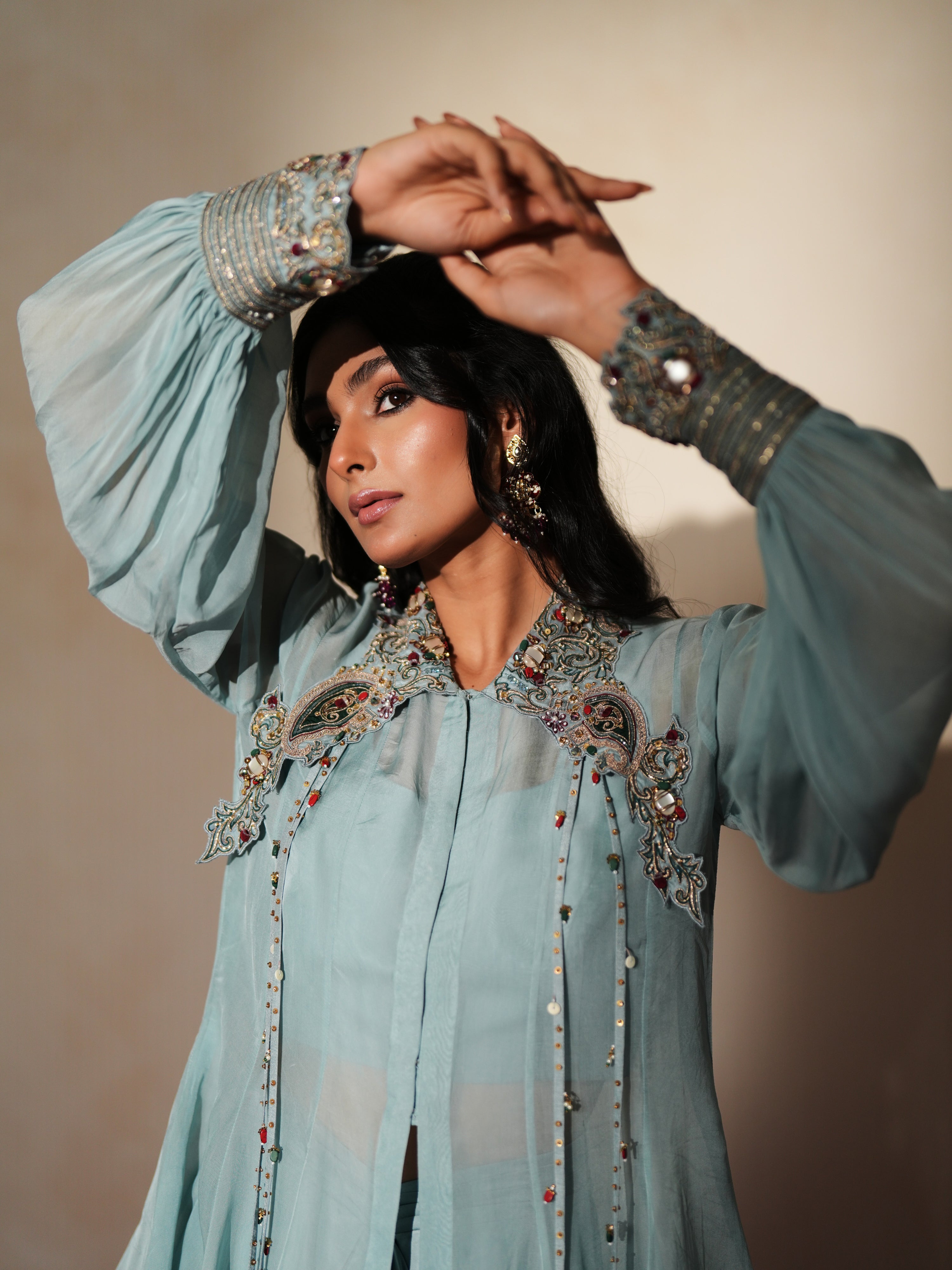 Woman in a pastel blue traditional outfit standing againsta beige wall on a red carpet.