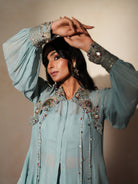Woman in a pastel blue traditional outfit standing againsta beige wall on a red carpet.