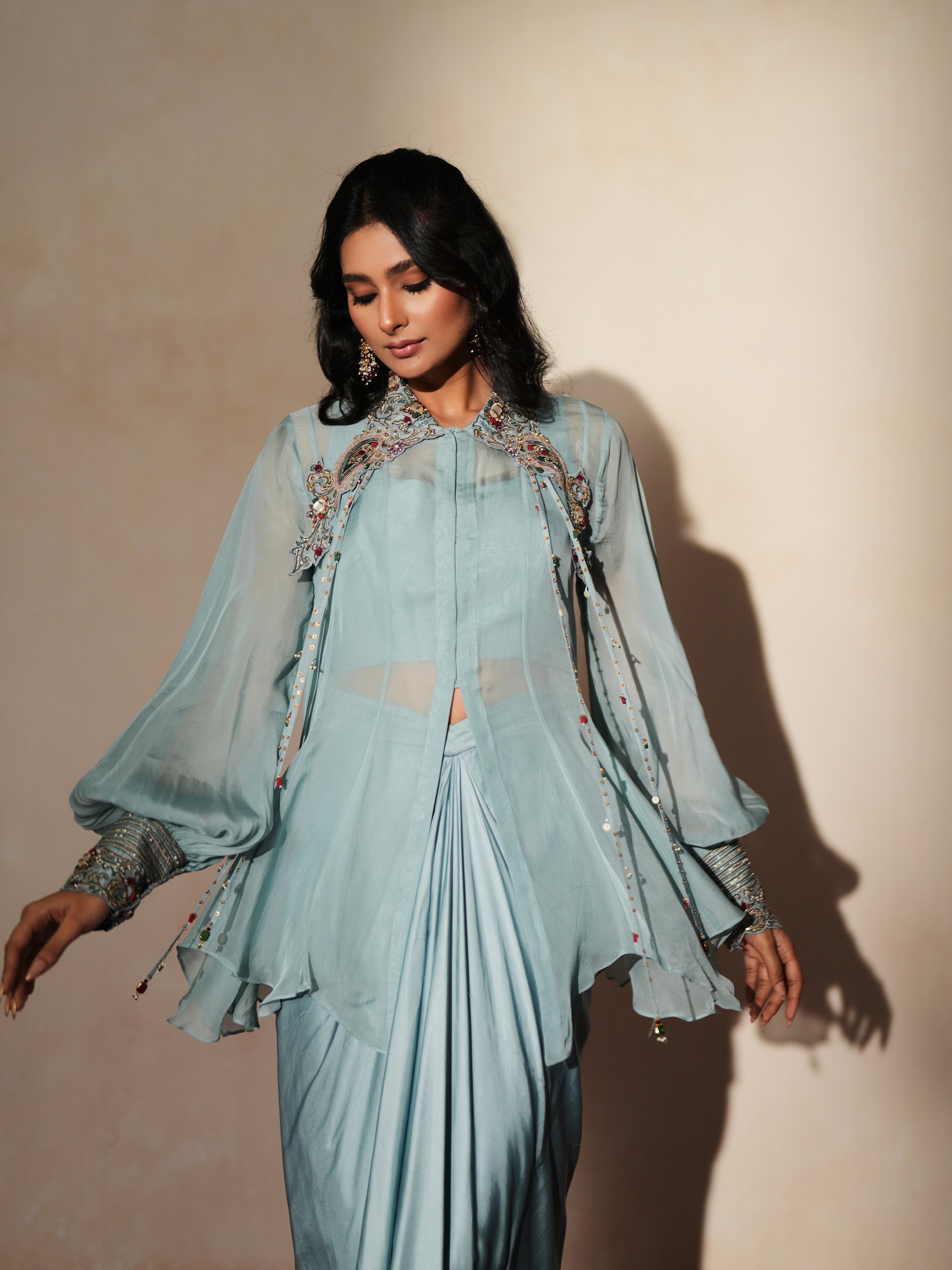 Woman in a pastel blue traditional outfit standing againsta beige wall on a red carpet.