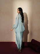 Woman in a pastel blue traditional outfit standing againsta beige wall on a red carpet.