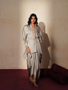 Woman in a mettalic grey traditional outfit standing againsta beige wall on a red carpet.