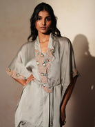 Woman in a mettalic grey traditional outfit standing againsta beige wall on a red carpet.