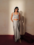 Woman in a mettalic grey traditional outfit standing againsta beige wall on a red carpet.