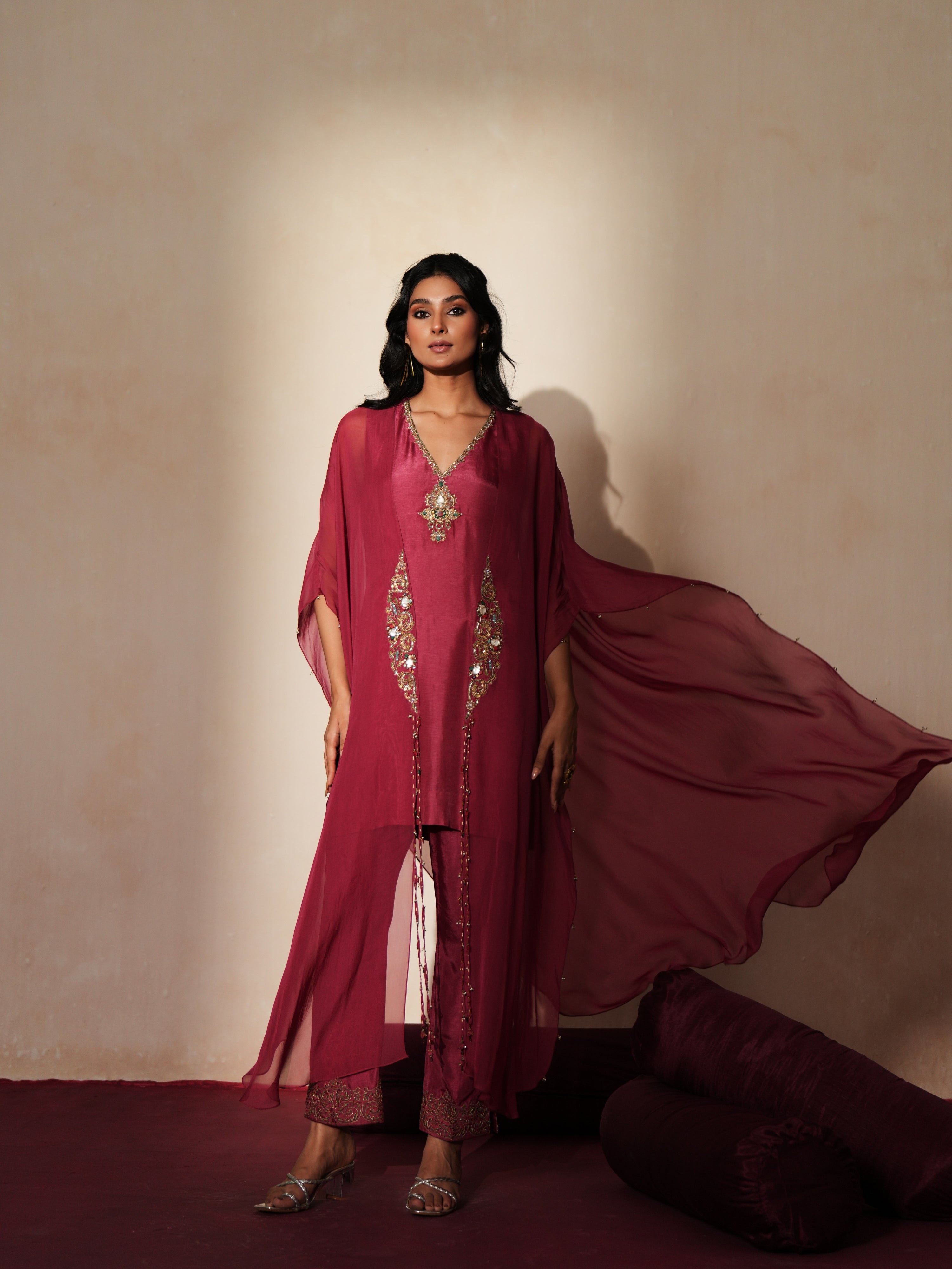 Woman in a mauve pink traditional outfit standing againsta beige wall on a red carpet.