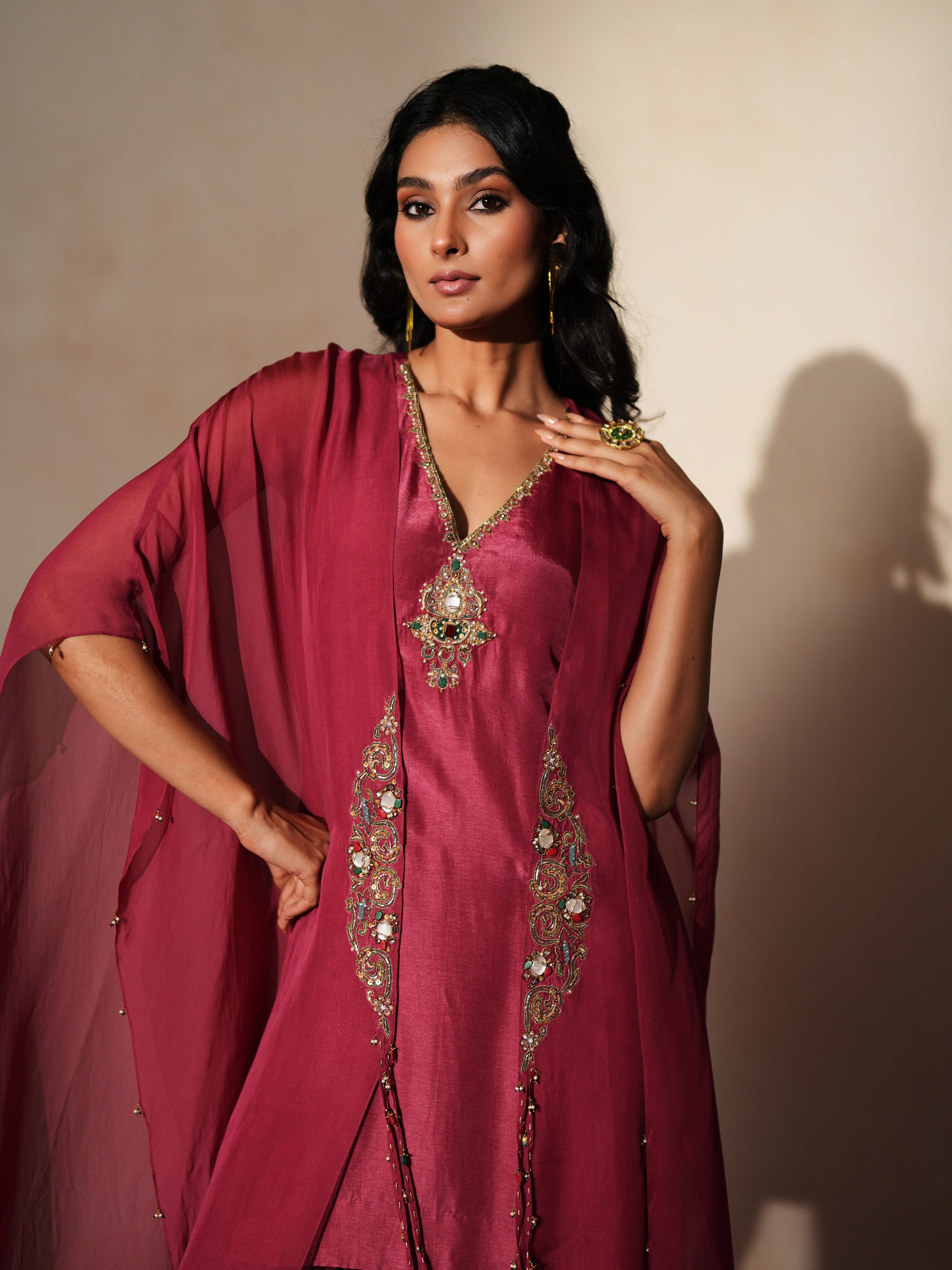 Woman in a mauve pink traditional outfit standing againsta beige wall on a red carpet.
