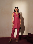 Woman in a mauve pink traditional outfit standing againsta beige wall on a red carpet.