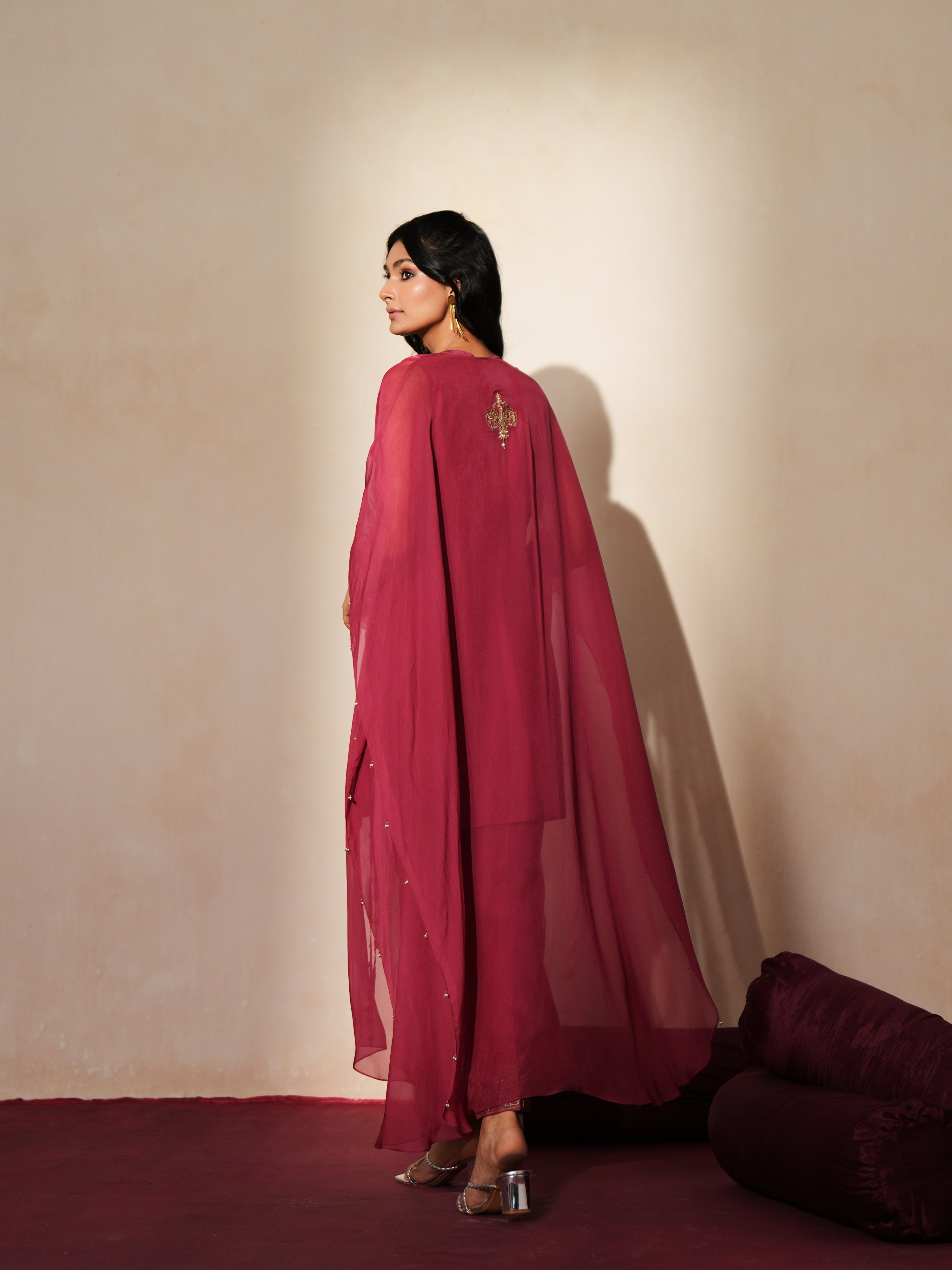 Woman in a mauve pink traditional outfit standing againsta beige wall on a red carpet.