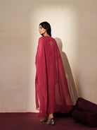 Woman in a mauve pink traditional outfit standing againsta beige wall on a red carpet.