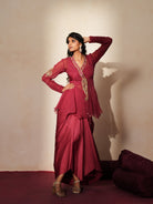 Woman in a mauve pink traditional outfit standing againsta beige wall on a red carpet.