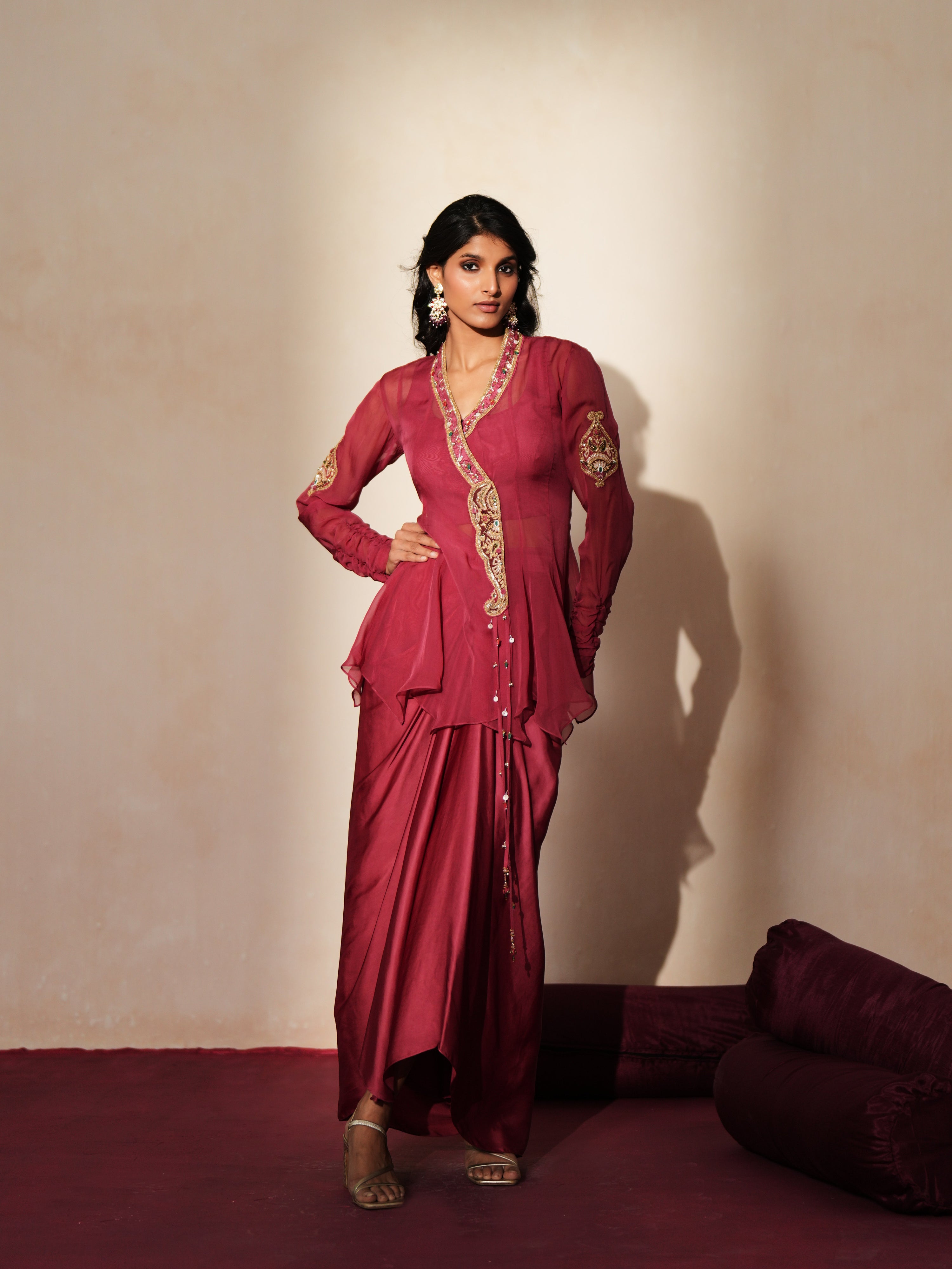 Woman in a mauve pink traditional outfit standing againsta beige wall on a red carpet.