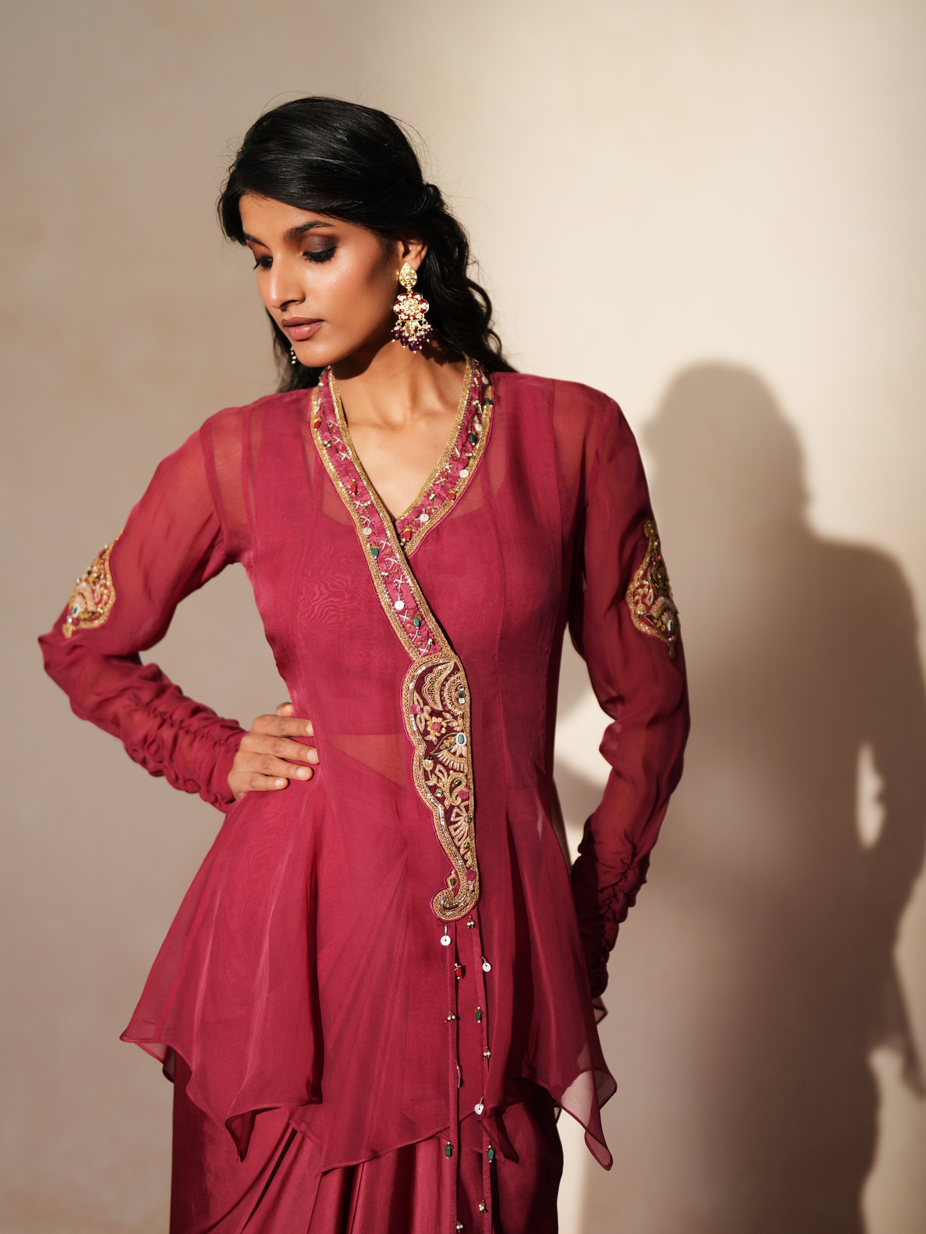 Woman in a mauve pink traditional outfit standing againsta beige wall on a red carpet.