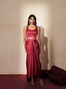 Woman in a mauve pink traditional outfit standing againsta beige wall on a red carpet.