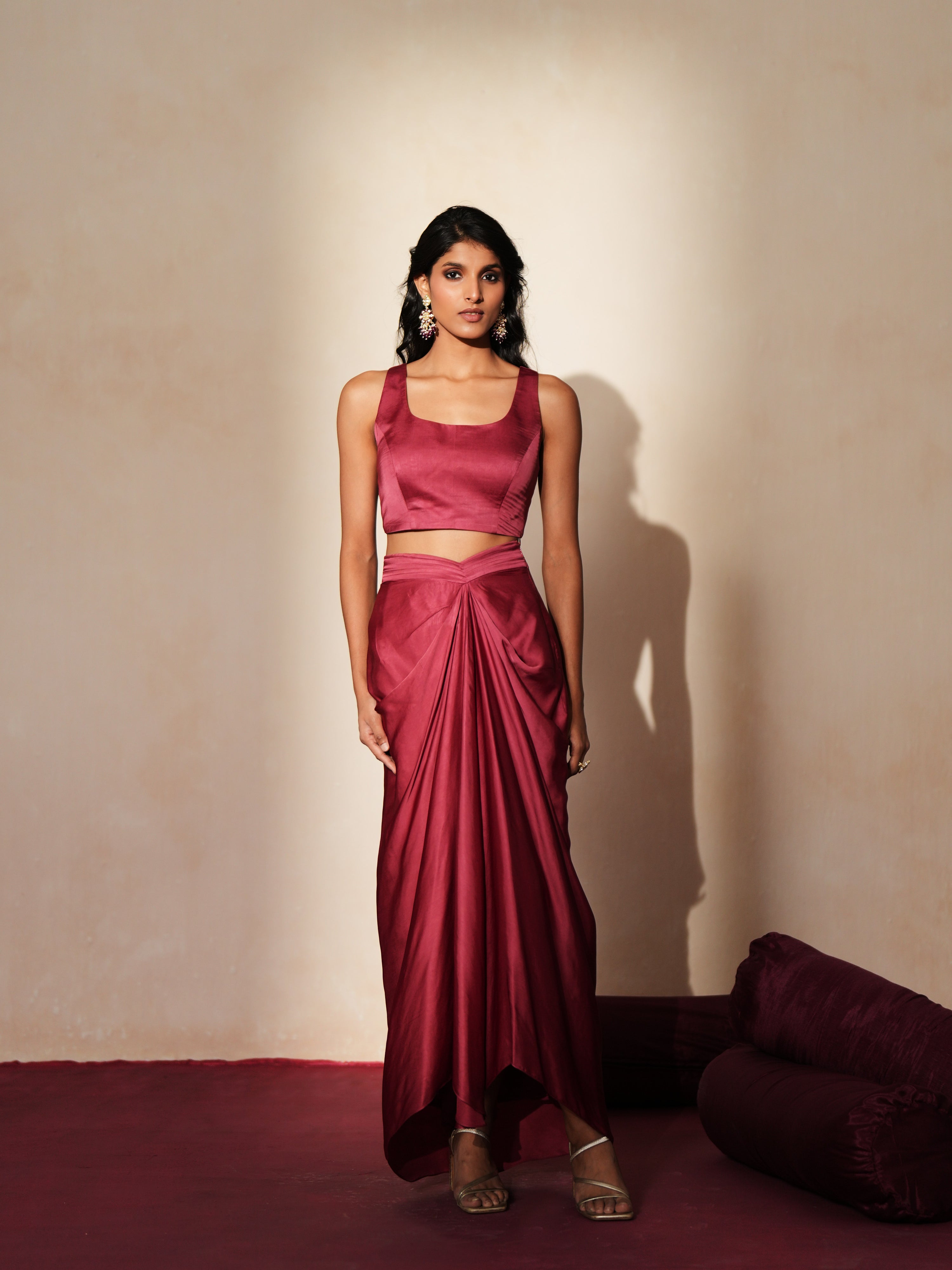 Woman in a mauve pink traditional outfit standing againsta beige wall on a red carpet.