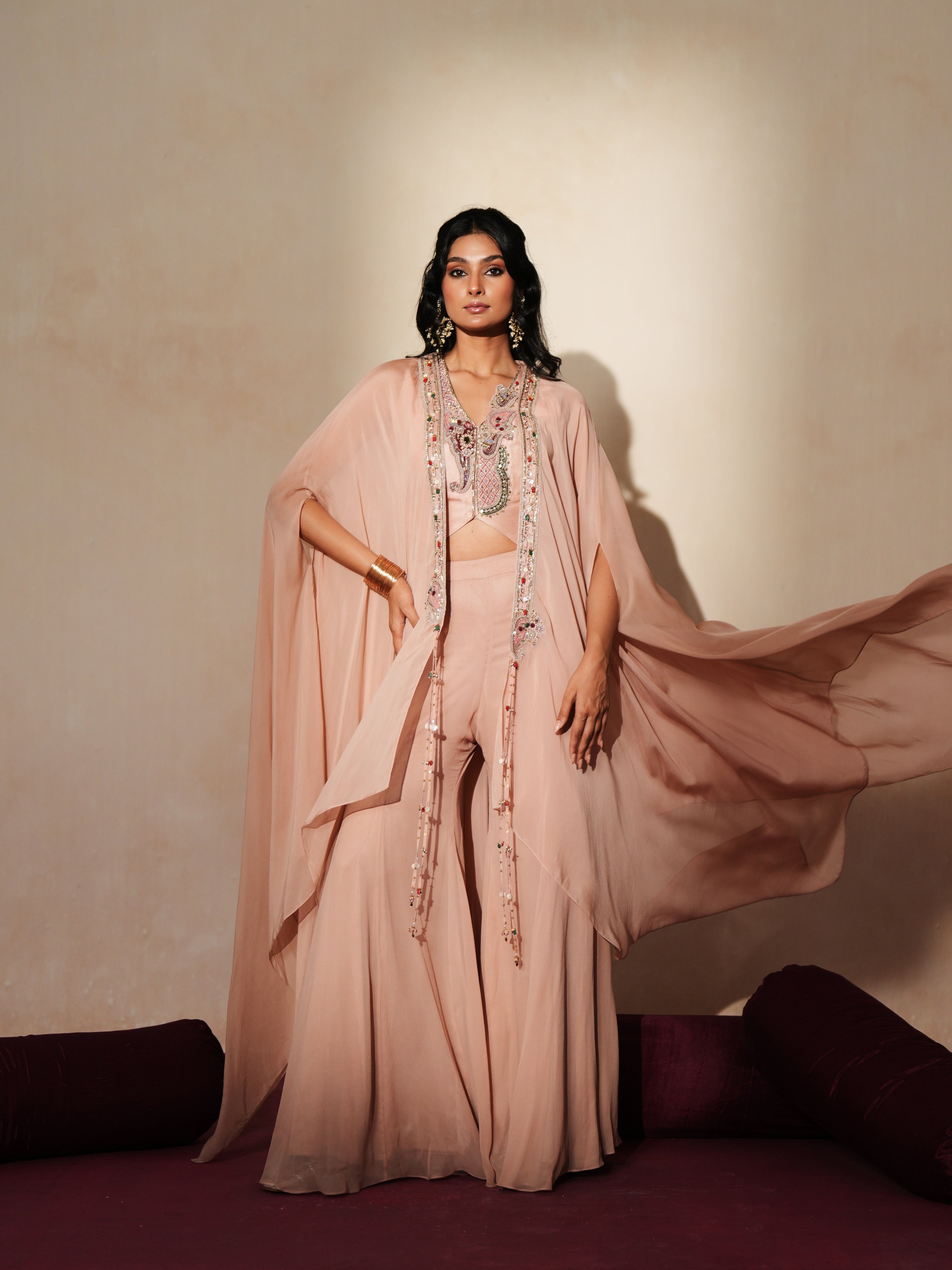 Woman in a soft pink traditional outfit standing againsta beige wall on a red carpet.