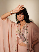 Woman in a soft pink traditional outfit standing againsta beige wall on a red carpet.