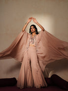 Woman in a soft pink traditional outfit standing againsta beige wall on a red carpet.