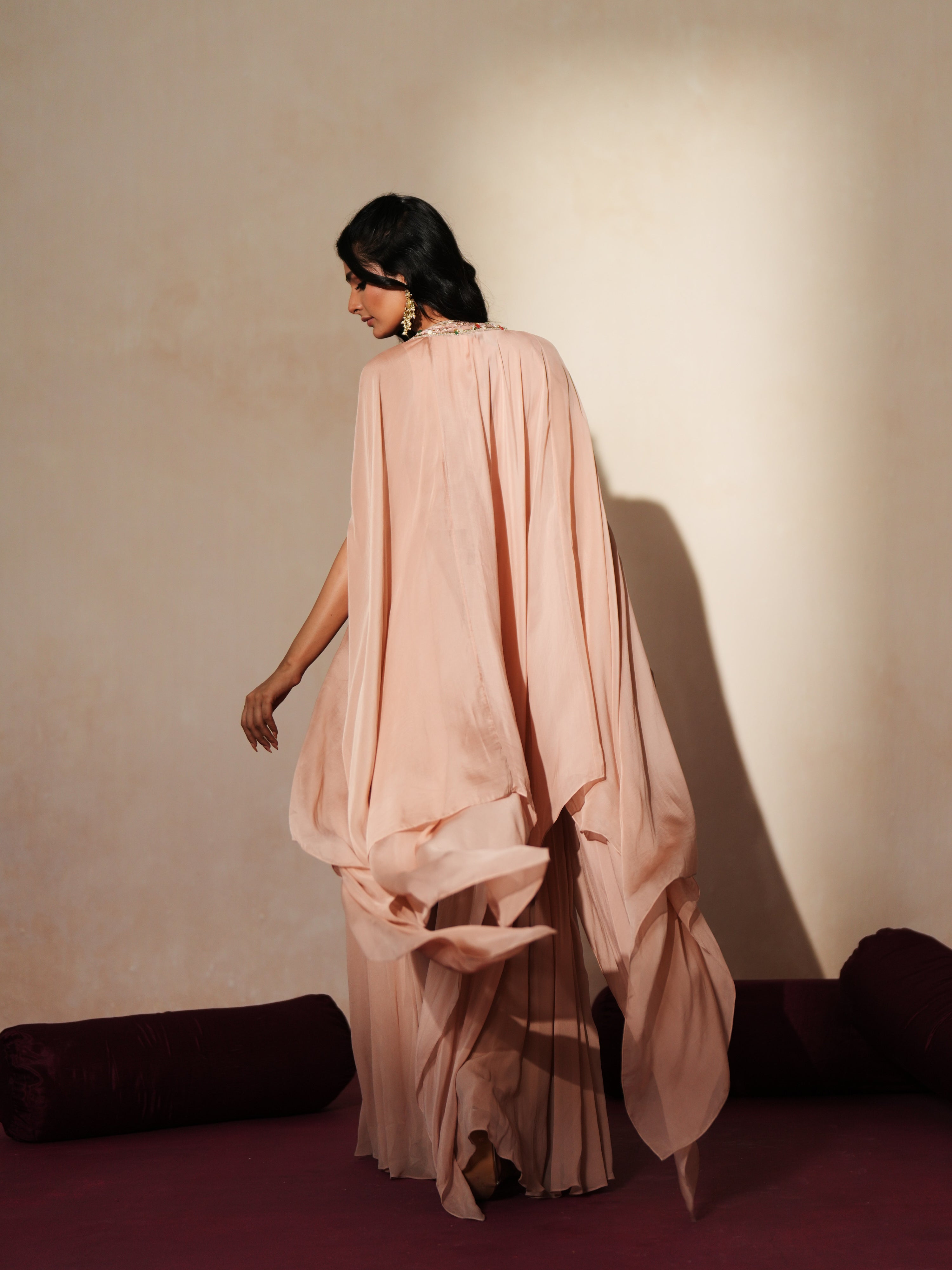 Woman in a soft pink traditional outfit standing againsta beige wall on a red carpet.