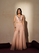 Woman in a soft pink traditional outfit standing againsta beige wall on a red carpet.