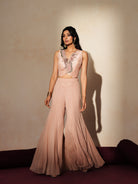 Woman in a soft pink traditional outfit standing againsta beige wall on a red carpet.