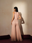 Woman in a soft pink traditional outfit standing againsta beige wall on a red carpet.